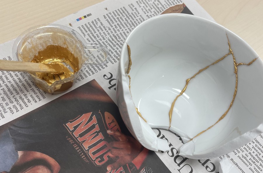 a broken white bowl is in the process of being being reassembled using a gold adhesive 